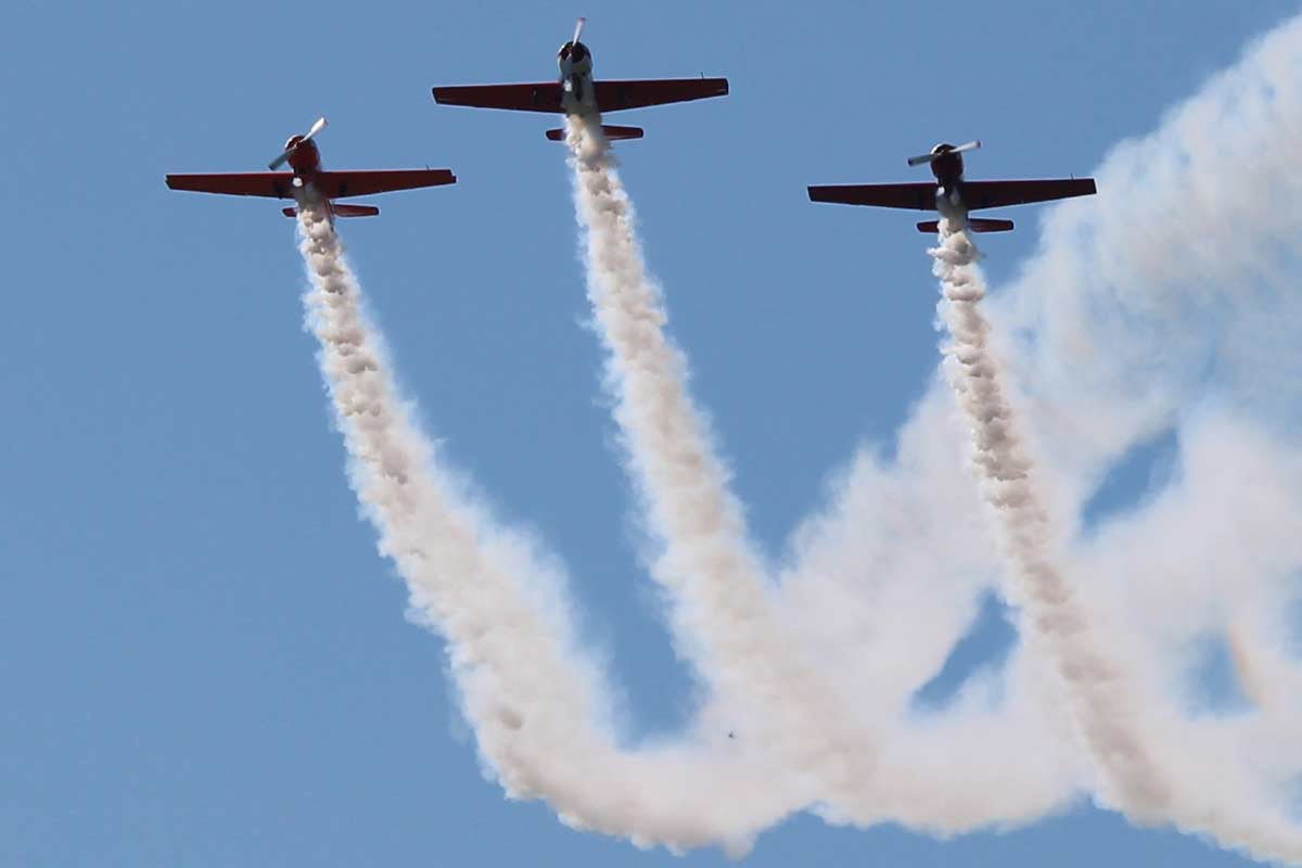 Mazury AirShow, trzy samoloty w kluczu ciągnące za sobą smugi dymu na błękitnym niebie